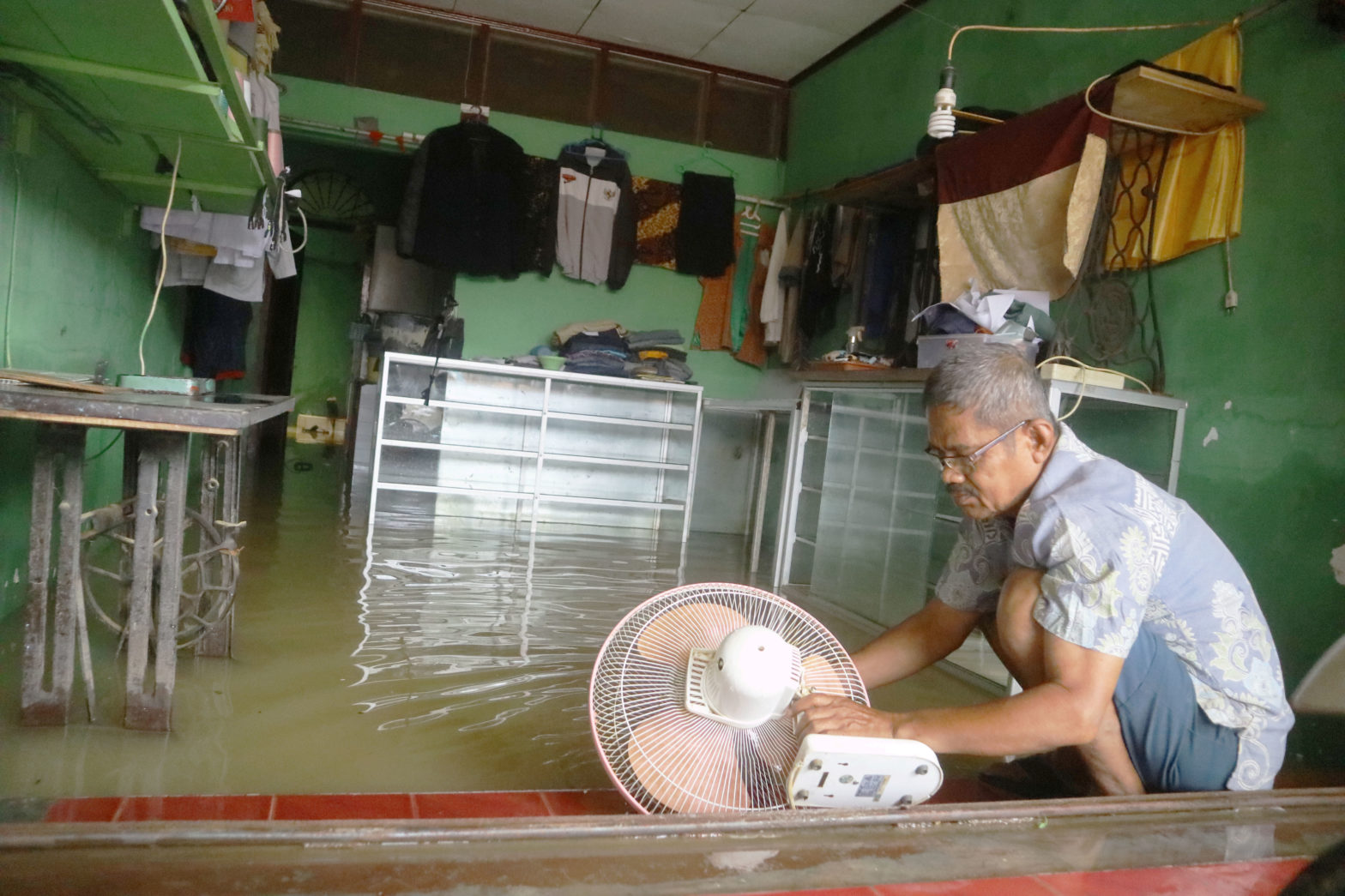 Mayunis (65) membersihkan kipas angin di kios jahitnya yang masih terendam