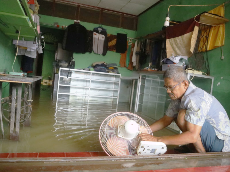 Mayunis (65) membersihkan kipas angin di kios jahitnya yang masih terendam